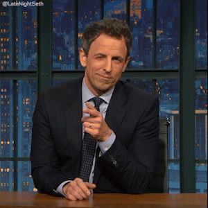 Apresentador de talk show sentado à bancada, com expressão curiosa