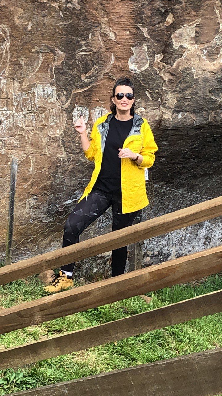 Beatriz Costa, de capa de chuva amarela, em frente a um painel de gravuras na rocha
