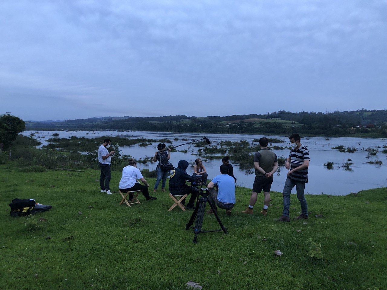 Equipe de filmagem reunida em um gramado à beira de um rio