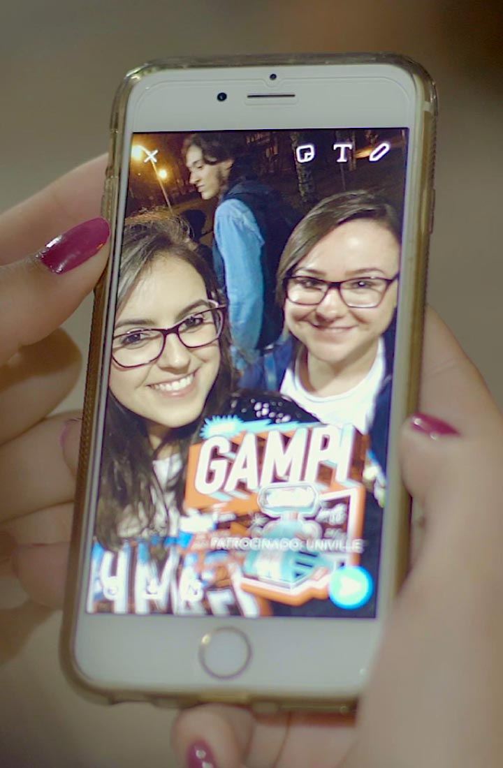 Selfie de estudantes com filtro da Univille na tela de um celular